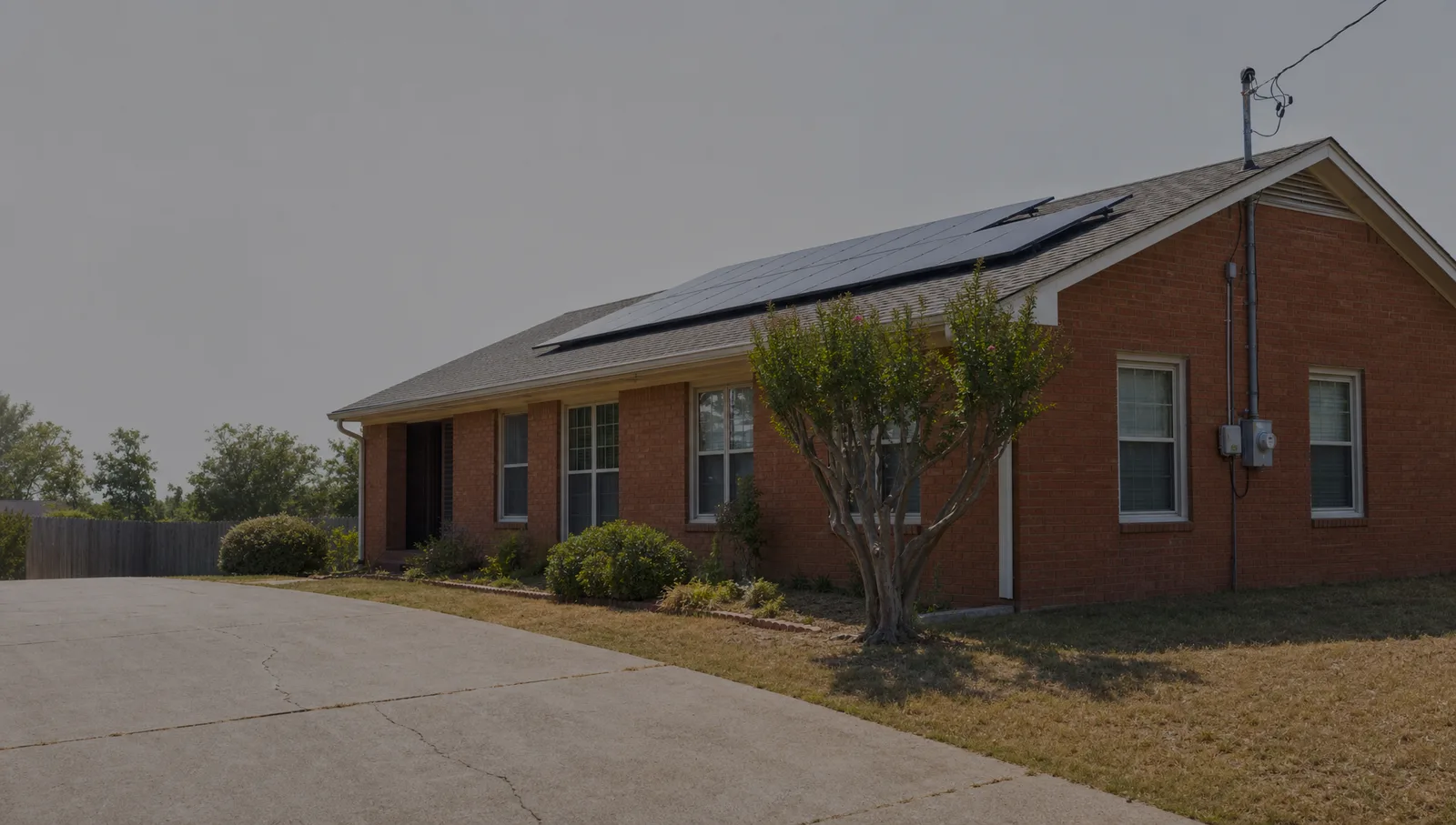 A single storey red brick ranch house in Memphis with solar modules on its low pitch shingle roof, seen from the driveway