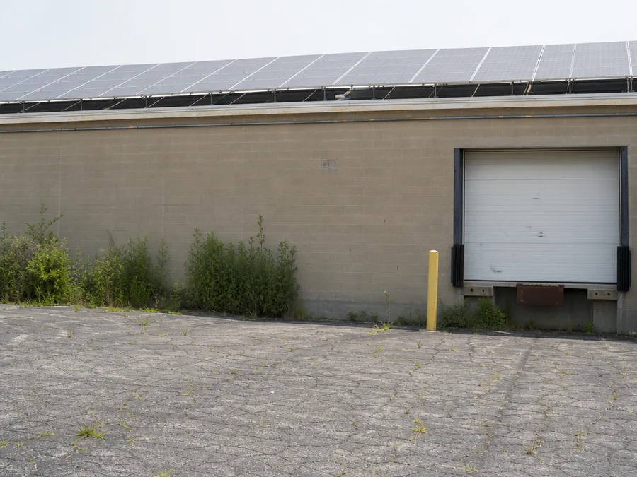 Solar modules standing above the flat roof line of a single storey block building, seen from its parking lot