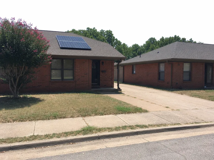 Two single storey brick ranch houses, one with a small solar array on its shingle roof and the next roof bare